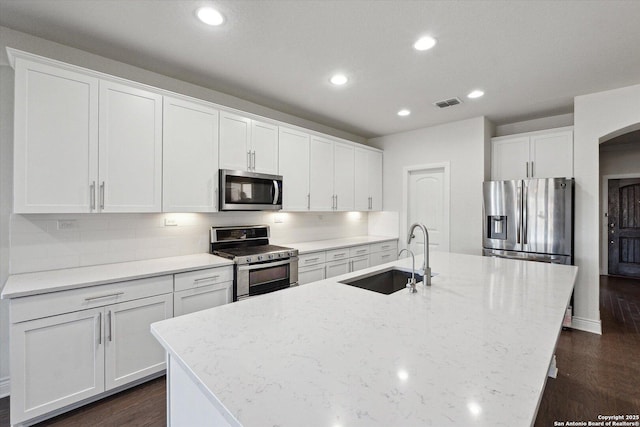 kitchen featuring visible vents, a kitchen island with sink, a sink, backsplash, and stainless steel appliances