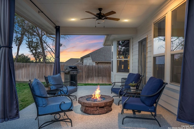 patio terrace at dusk featuring a grill, an outdoor fire pit, a ceiling fan, and fence