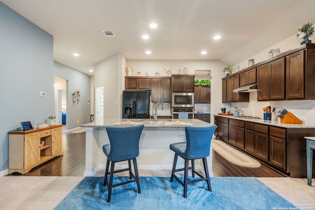 kitchen featuring under cabinet range hood, dark brown cabinetry, dark wood-style floors, stainless steel appliances, and a sink