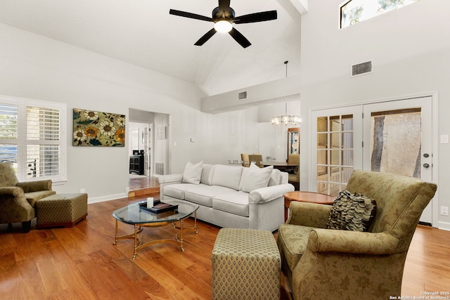 living room featuring wood finished floors, baseboards, visible vents, high vaulted ceiling, and ceiling fan with notable chandelier