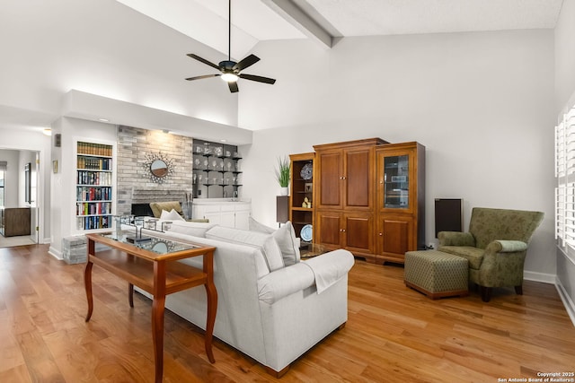 living area with beam ceiling, high vaulted ceiling, a brick fireplace, and light wood finished floors