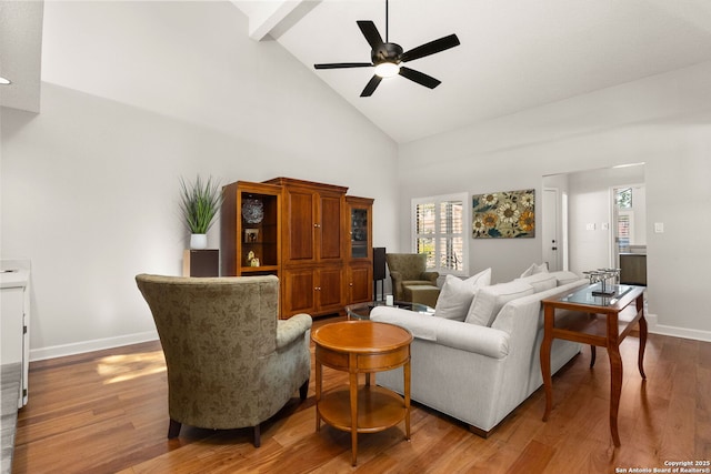 living area featuring a ceiling fan, wood finished floors, baseboards, high vaulted ceiling, and beam ceiling