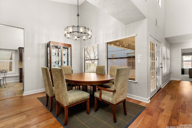 dining area featuring a notable chandelier, high vaulted ceiling, baseboards, and wood finished floors