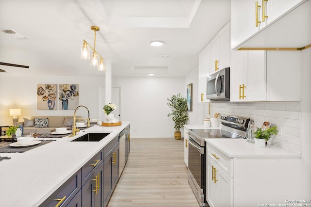 kitchen with a sink, stainless steel appliances, white cabinets, light countertops, and decorative backsplash