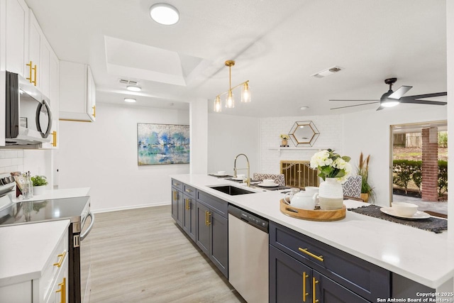 kitchen featuring a sink, stainless steel appliances, light countertops, white cabinets, and a brick fireplace