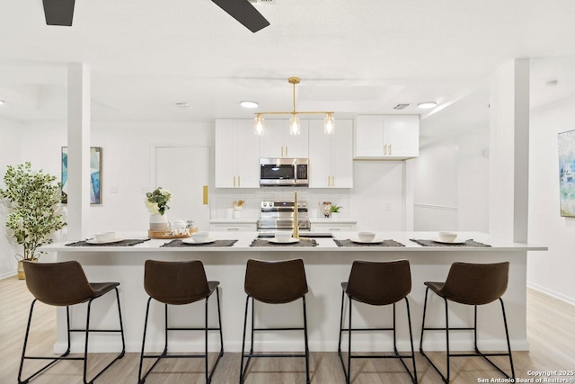 kitchen featuring light wood-type flooring, a kitchen bar, backsplash, appliances with stainless steel finishes, and white cabinets