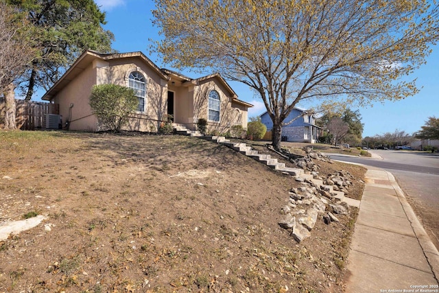 view of front facade featuring stucco siding, central AC, and fence