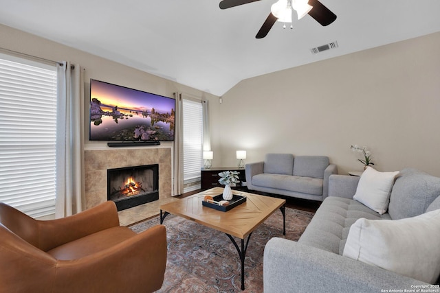 living room with ceiling fan, vaulted ceiling, visible vents, and a tile fireplace