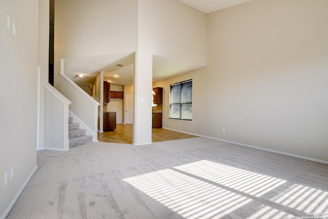 carpeted empty room featuring baseboards, stairs, and a towering ceiling