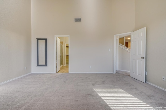 unfurnished bedroom featuring visible vents, light carpet, ensuite bathroom, baseboards, and a towering ceiling