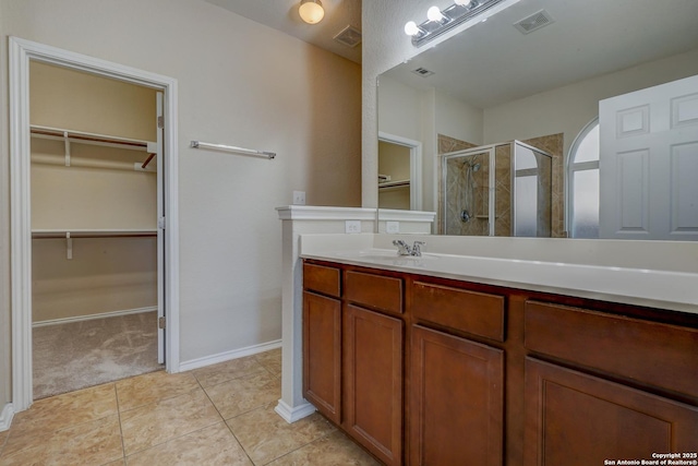 bathroom featuring visible vents, a shower stall, a walk in closet, tile patterned floors, and vanity