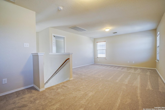 spare room featuring a textured ceiling, visible vents, baseboards, and light carpet