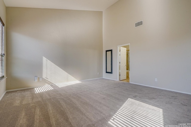 carpeted empty room with visible vents, a high ceiling, and baseboards