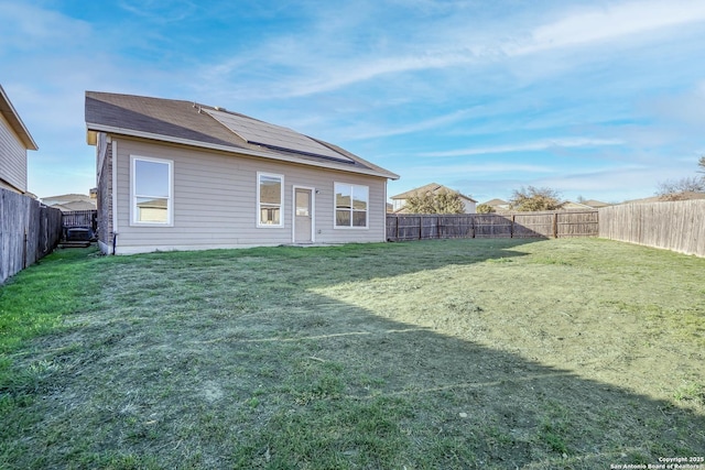 back of property with a fenced backyard, roof mounted solar panels, and a yard