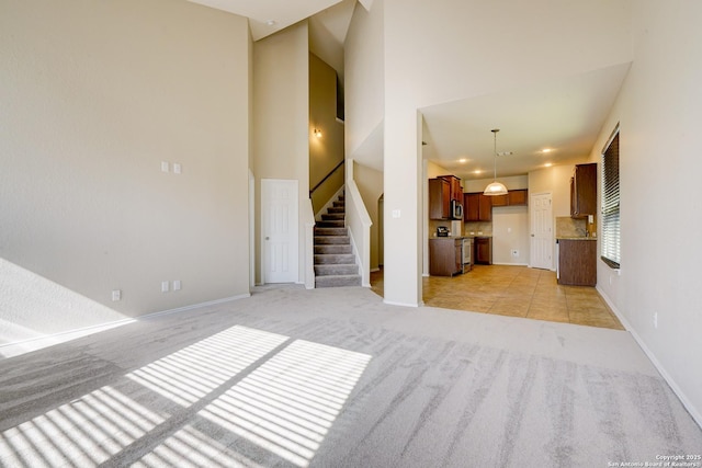 unfurnished living room featuring stairs, light colored carpet, and baseboards