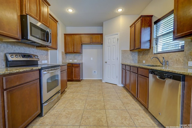 kitchen featuring light tile patterned floors, light stone counters, brown cabinets, stainless steel appliances, and a sink