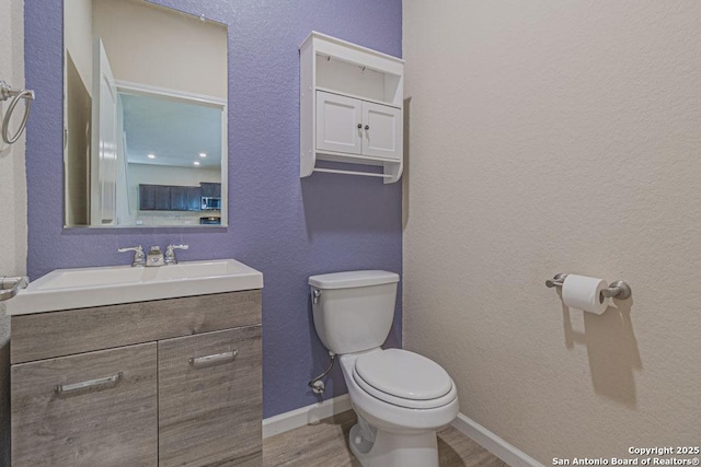 bathroom with vanity, wood finished floors, baseboards, toilet, and a textured wall