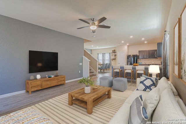 living area featuring stairway, a ceiling fan, visible vents, baseboards, and light wood-style floors