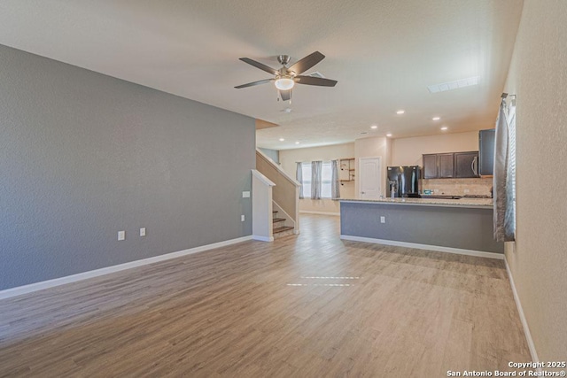 unfurnished living room featuring baseboards, a ceiling fan, stairs, and light wood finished floors