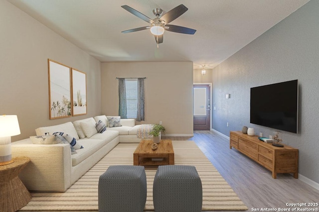 living room with ceiling fan, baseboards, and light wood-style floors