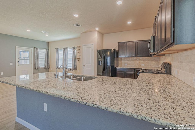 kitchen with tasteful backsplash, range with gas cooktop, light stone countertops, black fridge, and a sink