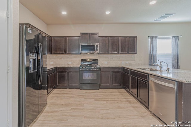 kitchen featuring visible vents, black appliances, a sink, light stone counters, and dark brown cabinets