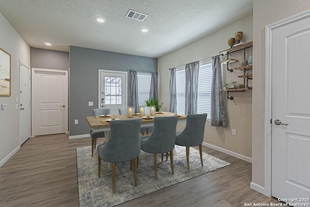 dining area with visible vents, a textured ceiling, baseboards, and wood finished floors