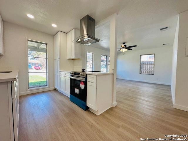 kitchen featuring light countertops, wall chimney range hood, light wood-style floors, and stainless steel range with electric cooktop