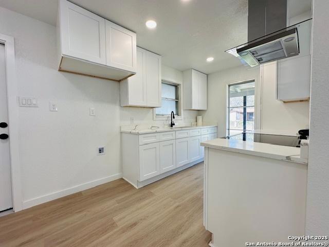 kitchen featuring ventilation hood, light wood-type flooring, light countertops, white cabinetry, and a sink