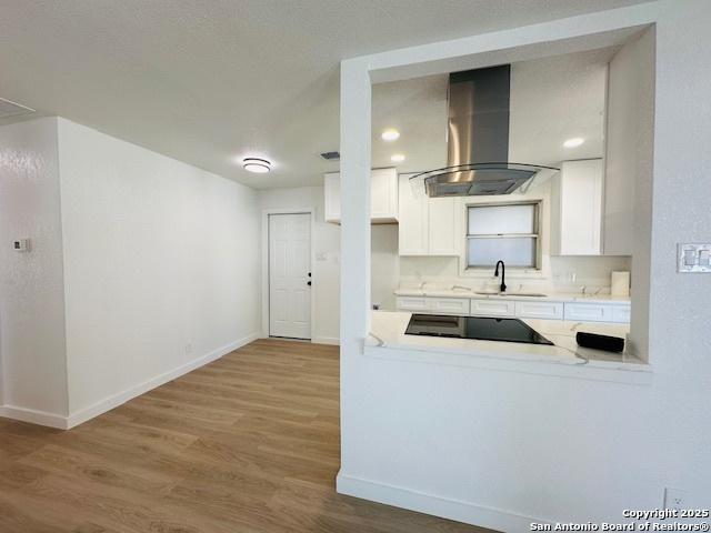 kitchen featuring wood finished floors, a sink, white cabinetry, black electric stovetop, and exhaust hood