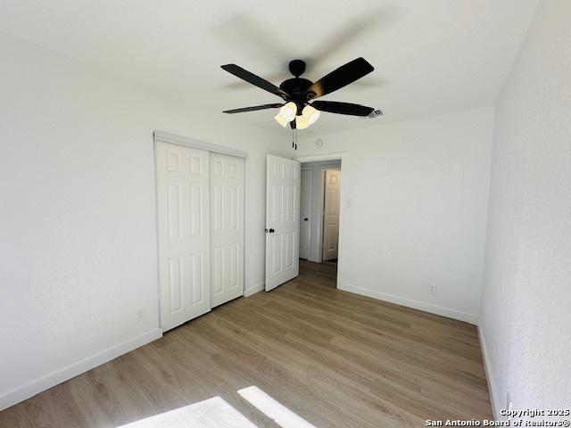 unfurnished bedroom featuring wood finished floors, baseboards, a closet, and ceiling fan