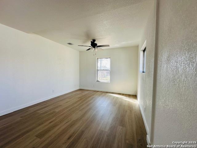 spare room with a ceiling fan, visible vents, wood finished floors, and baseboards