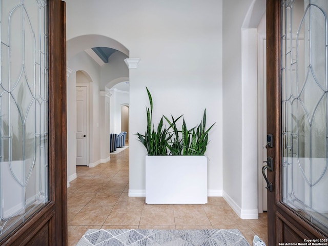 foyer featuring light tile patterned floors, baseboards, and arched walkways