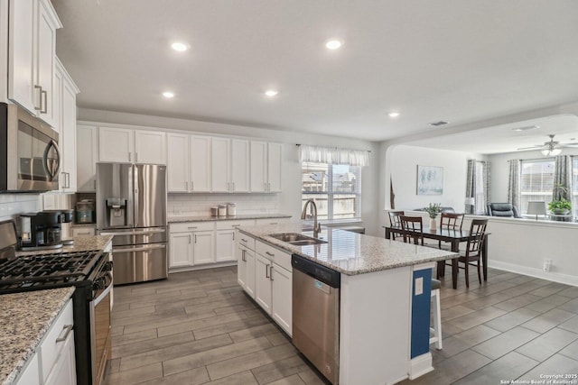 kitchen with wood finish floors, a sink, stainless steel appliances, white cabinets, and backsplash