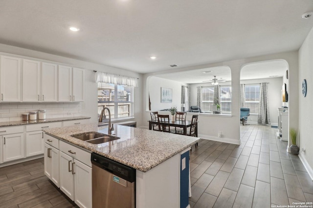 kitchen with wood tiled floor, arched walkways, a sink, stainless steel dishwasher, and backsplash