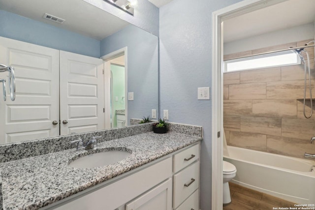 bathroom featuring visible vents, toilet, shower / washtub combination, wood finished floors, and vanity