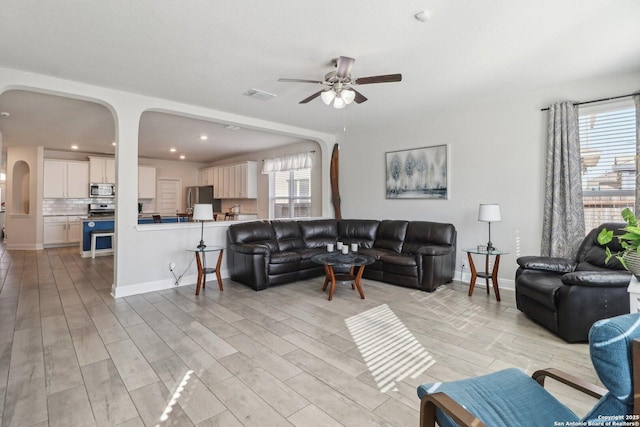 living room with visible vents, arched walkways, light wood finished floors, baseboards, and ceiling fan