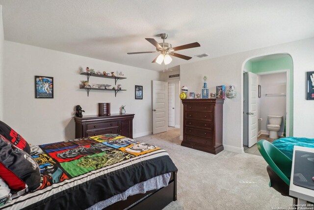 bedroom featuring visible vents, baseboards, light carpet, ensuite bathroom, and arched walkways