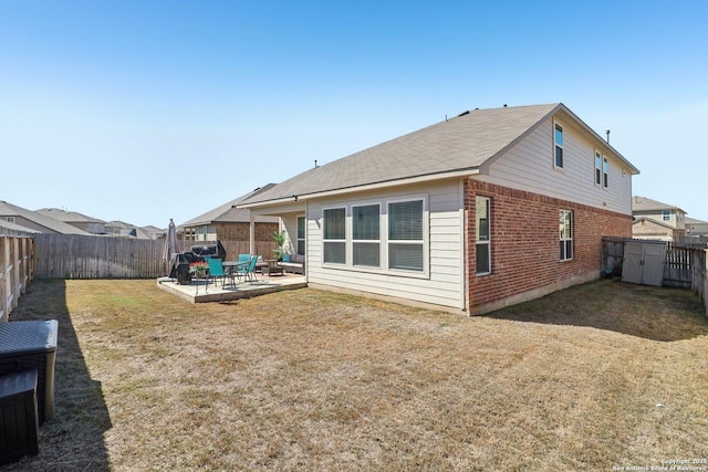 rear view of house with a patio, brick siding, a fenced backyard, and a lawn