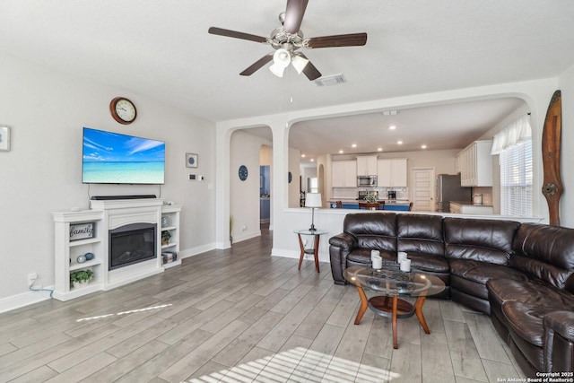 living room featuring light wood finished floors, visible vents, baseboards, arched walkways, and a glass covered fireplace