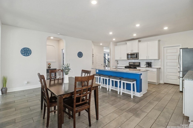 dining room featuring arched walkways, recessed lighting, light wood-style flooring, and baseboards