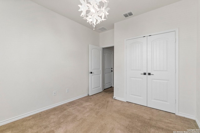 unfurnished bedroom with visible vents, baseboards, light carpet, a closet, and a notable chandelier