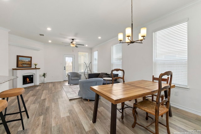 dining room featuring light wood finished floors, a warm lit fireplace, baseboards, and ornamental molding