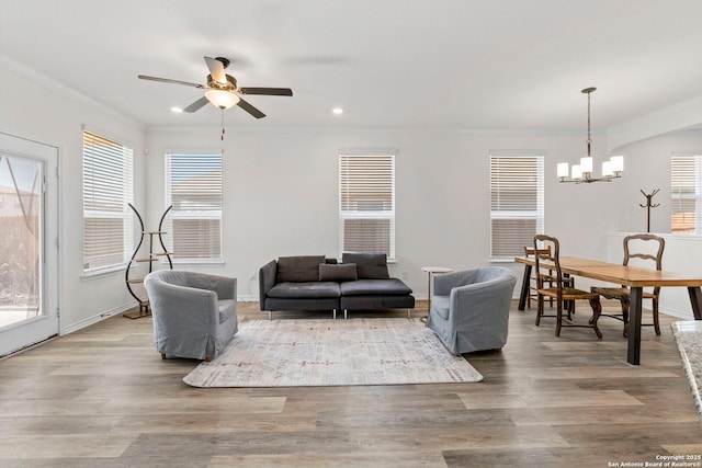 living room with ornamental molding, ceiling fan with notable chandelier, wood finished floors, recessed lighting, and baseboards