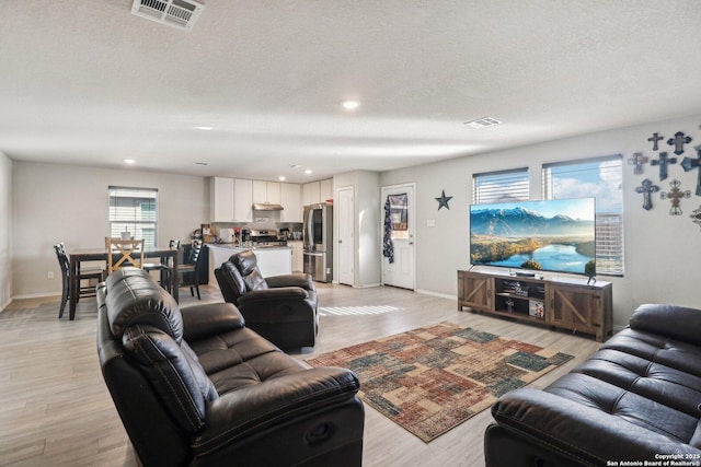 living area with light wood-style flooring, baseboards, visible vents, and a textured ceiling