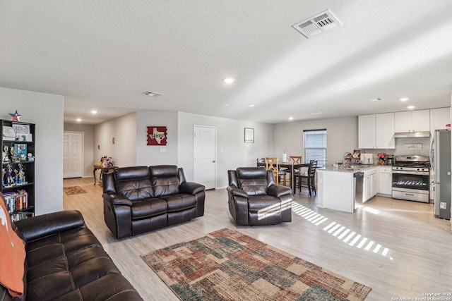 living room featuring recessed lighting, visible vents, a textured ceiling, and light wood finished floors