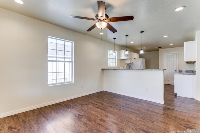 kitchen with dark wood-type flooring, freestanding refrigerator, a peninsula, white cabinets, and light stone countertops