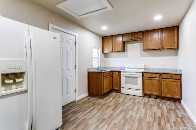 kitchen with light stone countertops, light wood-style floors, brown cabinetry, white appliances, and a sink