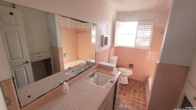 bathroom featuring wainscoting, a washtub, toilet, and brick floor