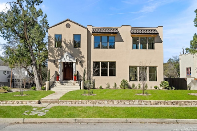 view of front facade featuring a front yard, fence, a tile roof, and stucco siding